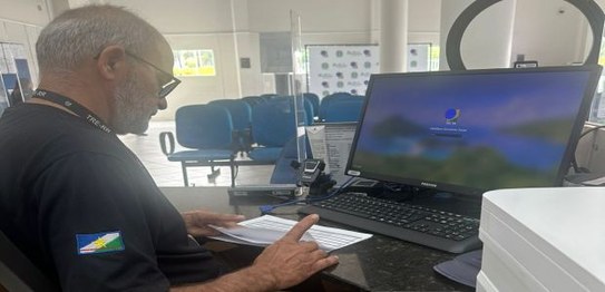 Na foto, 3 pessoas aparecem trabalhando. São 2 homens sentados em frente a tela de computadores ...