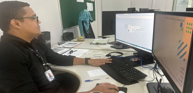 Na foto, homem jovem aparece de frente para duas telas de computador. Em uma das telas, imagem d...